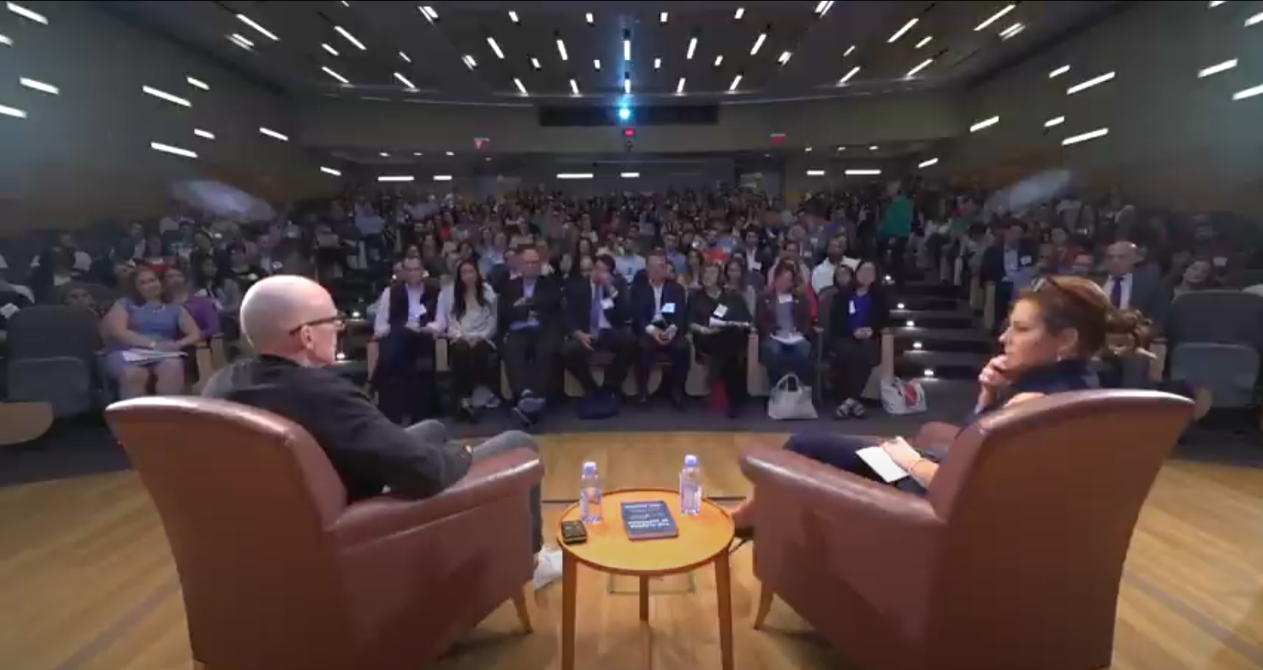 Scott Galloway and Stephanie Rhule sitting on stage in front of an audience